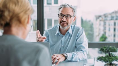 A financial adviser smiles as he speaks with a client in his office.
