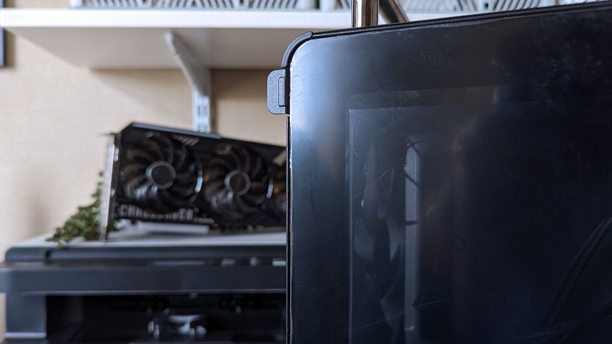 Cooler Master Qube 340 PC case glass side panel tab photographed close up with a triple-fan graphics card in the background