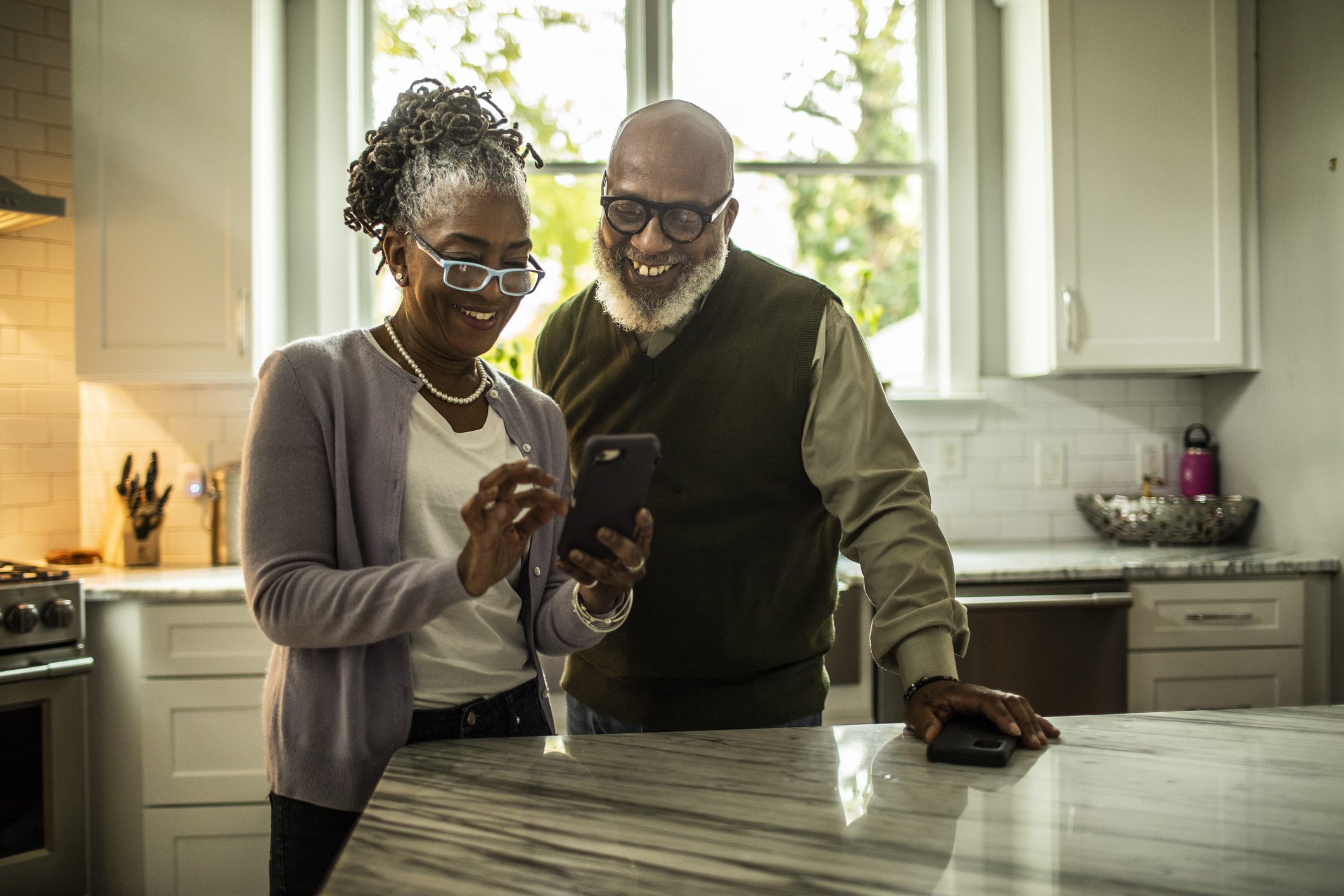 Senior couple using smartphone in kitchen of suburban home