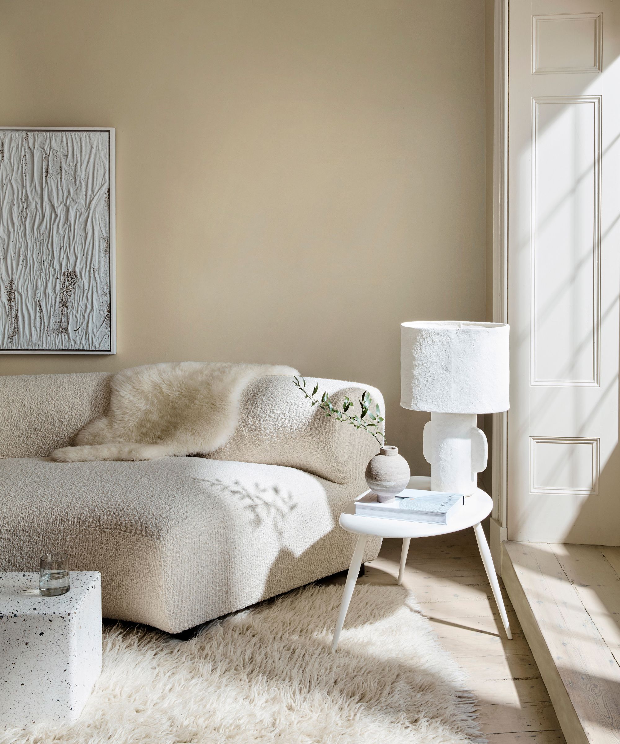 corner of neutral living room with beige walls, cream bouclé sofa, and light-flooded window
