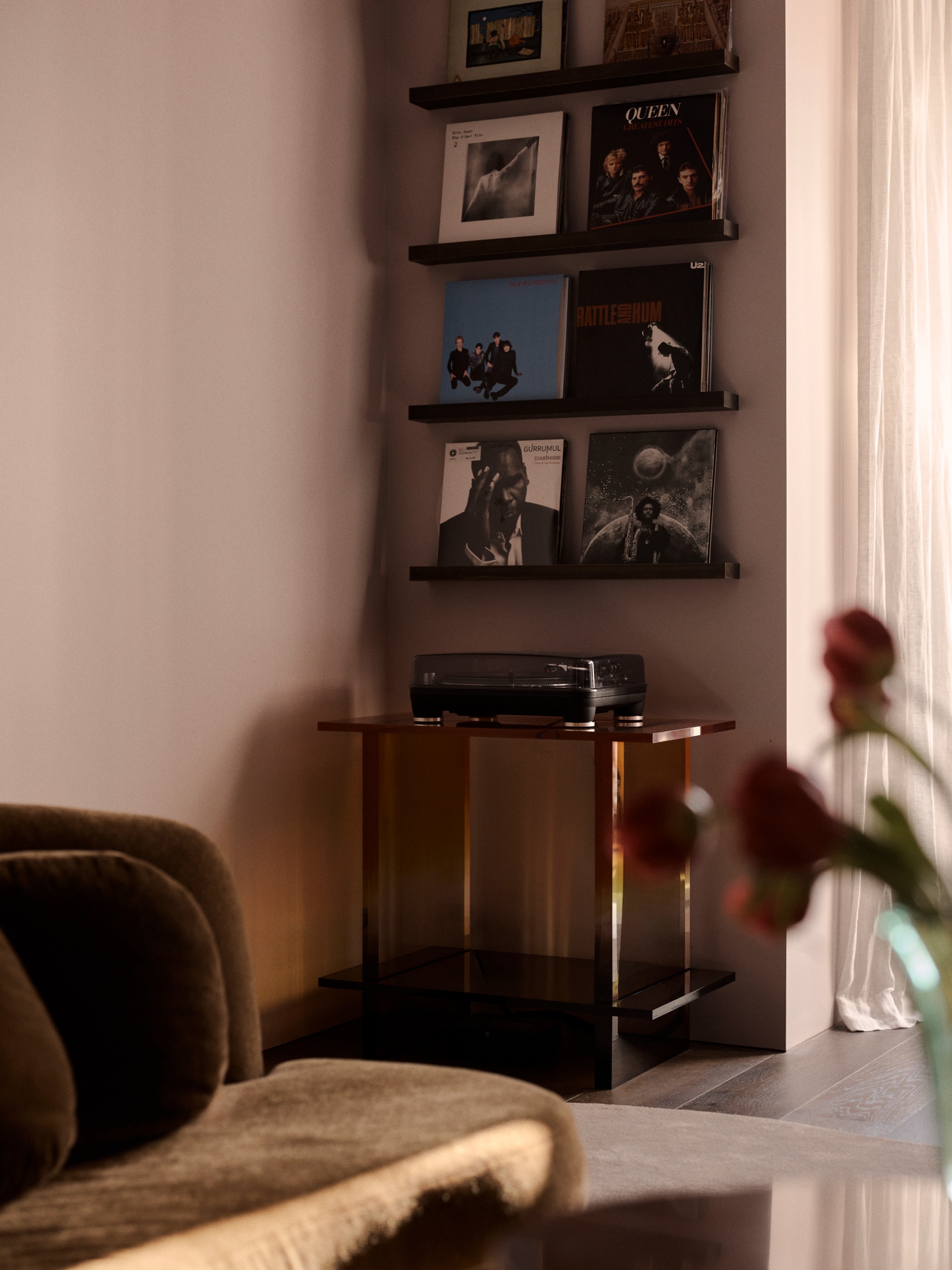 a pink-toned living area with a record player on a perspex table and a display of records