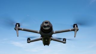 DJI Mavic 4 Pro in flight against a blue sky facing towards the camera with the drone camera and gimbal visible