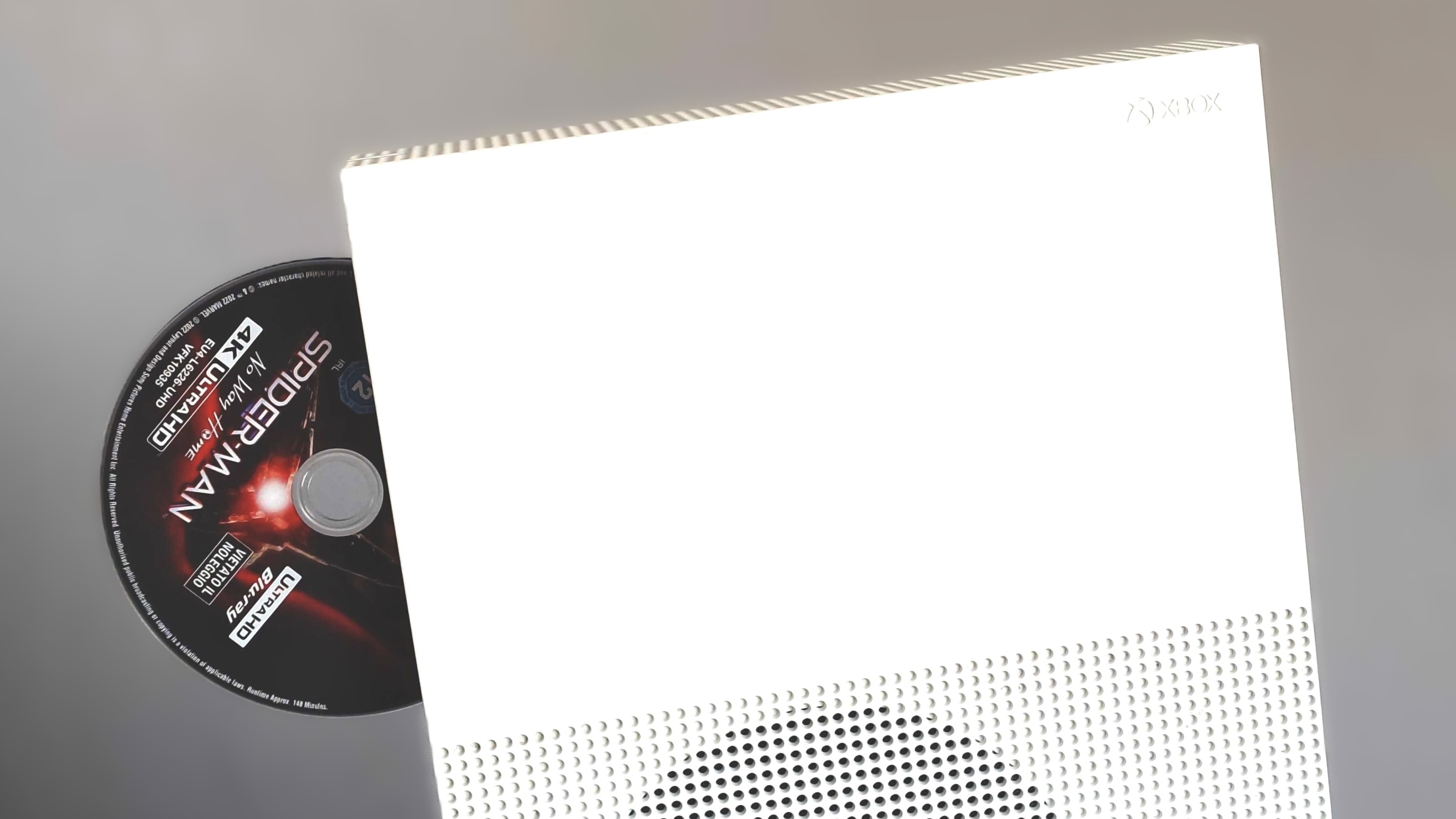 A white Xbox One S stood up with a Spider-Man: No Way Home 4K Ultra HD Blu-Ray disc ejected from its drive.