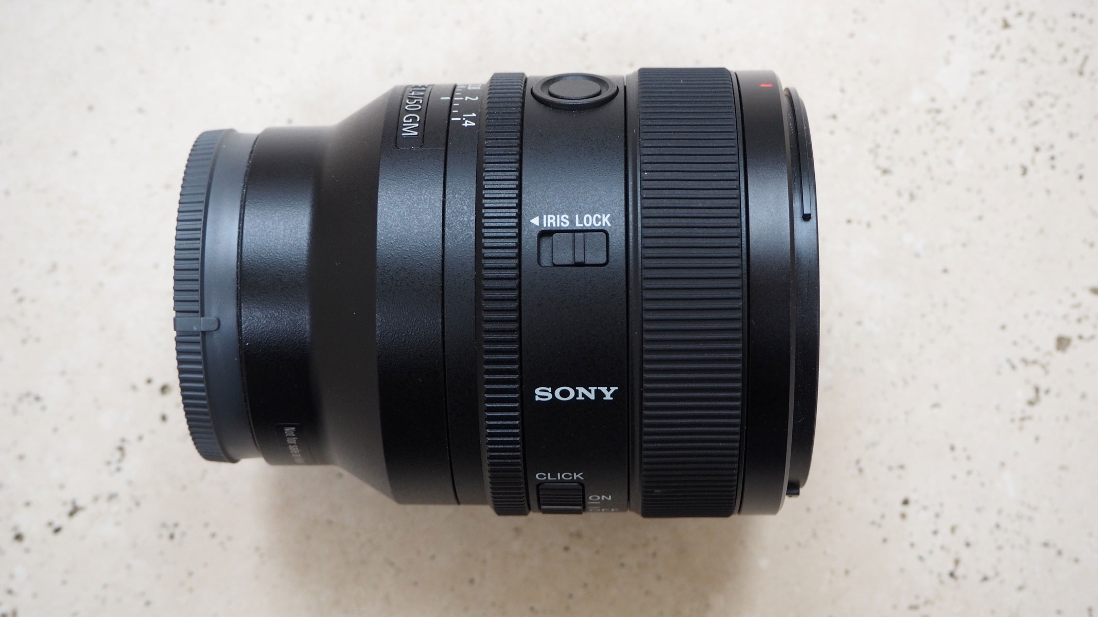 A side view of the Sony 50mm f/1.4 GM lens on a table.