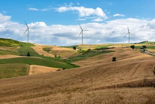 Row of wind turbines in a wind farm on the hilltops viewed across rolling agricultural land in a concept of alternative power