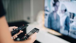 Person holding up remotes to TV screen