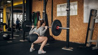 Woman performing a barbell back squat in the gym in a squat position