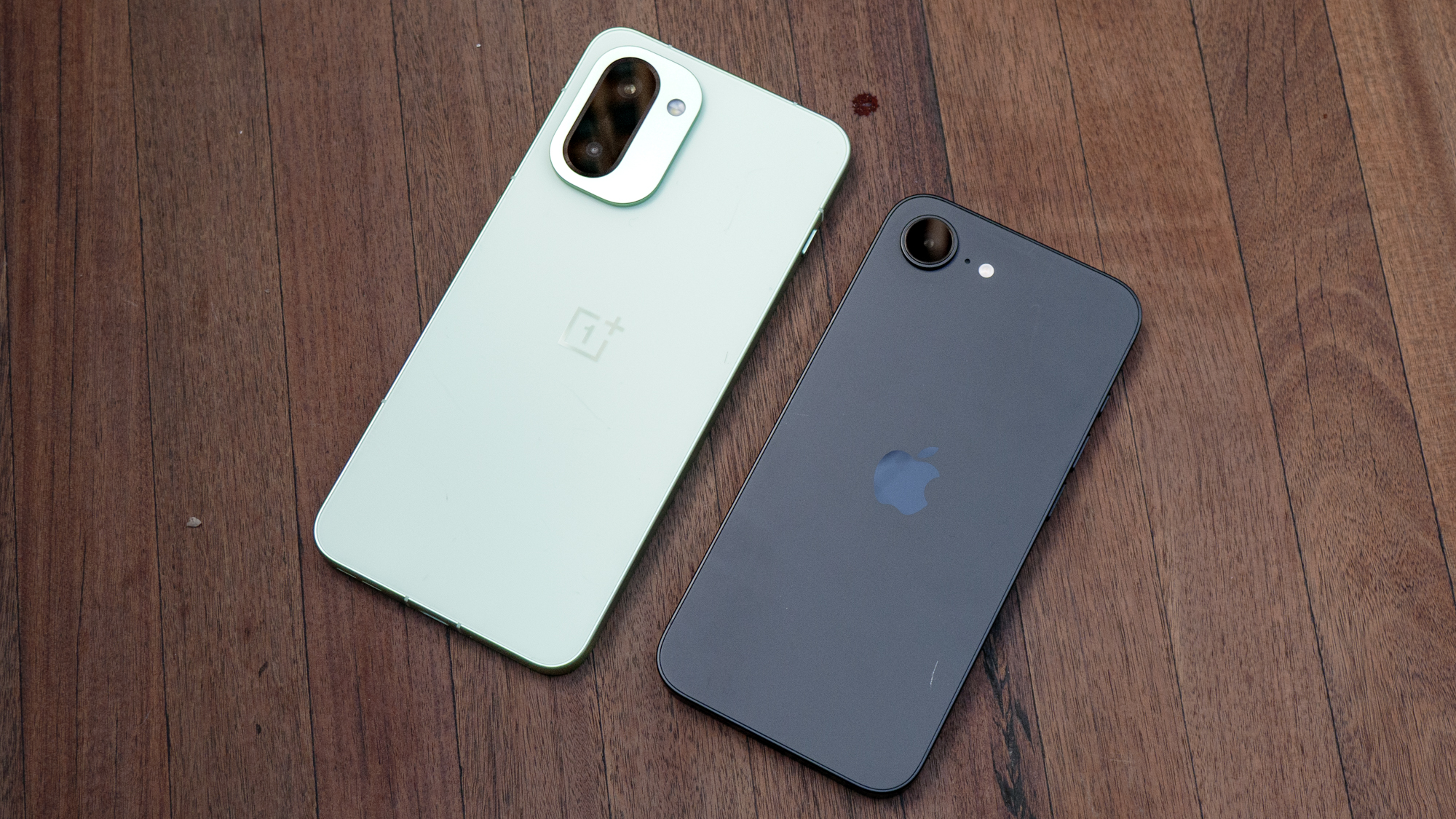 OnePlus 15R vs iPhone 16e on wooden surface.