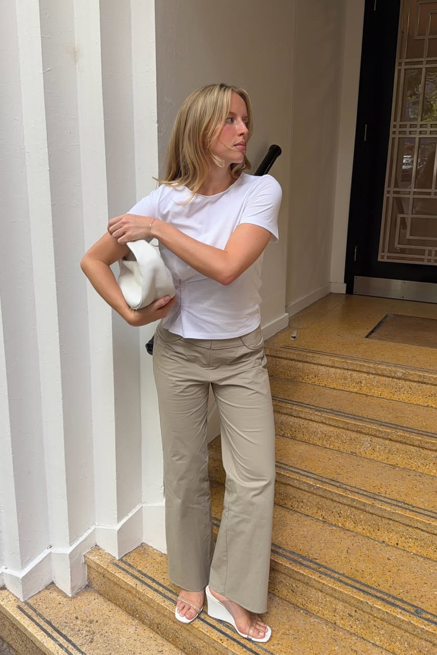 a woman wearing a white t-shirt, beige pants, white wedge sandals, and white purse