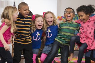 nursery children standing with their arms around each other and laughing as they face the camera