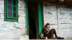Woman sat writing in a notebook outside a wooden hut.