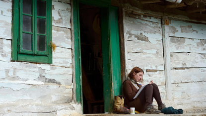 Woman sat writing in a notebook outside a wooden hut.
