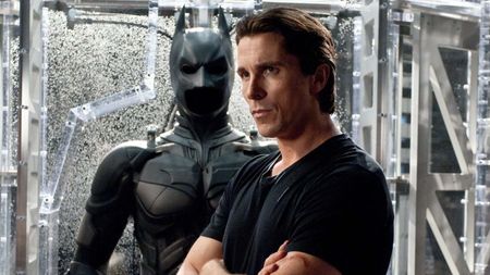 Bruce Wayne stands in front of the Batsuit
