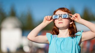 Young girl with red hair watching the annular solar eclipse with special viewing glasses.