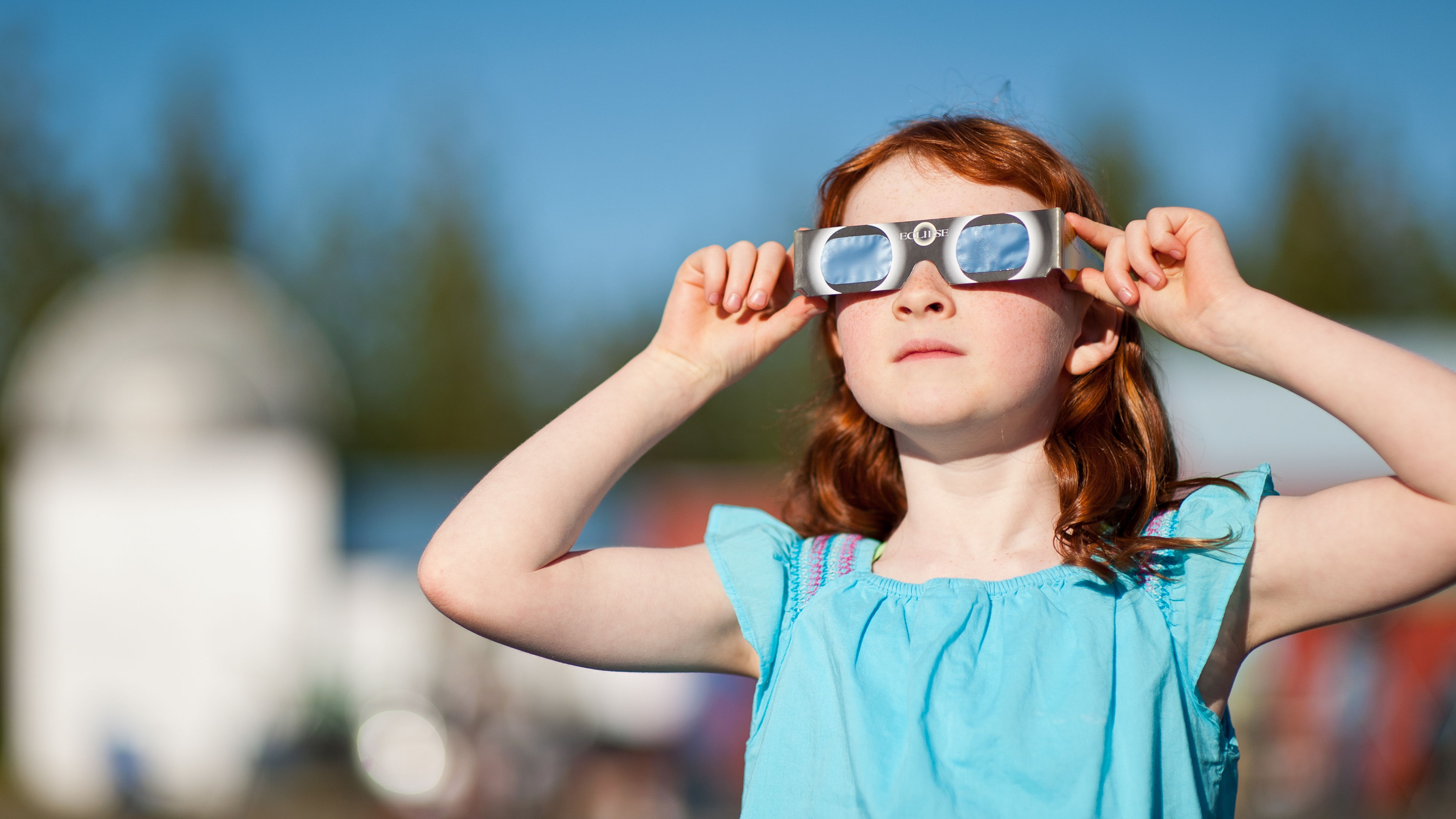 Young girl with red hair watching the annular solar eclipse with special viewing glasses.