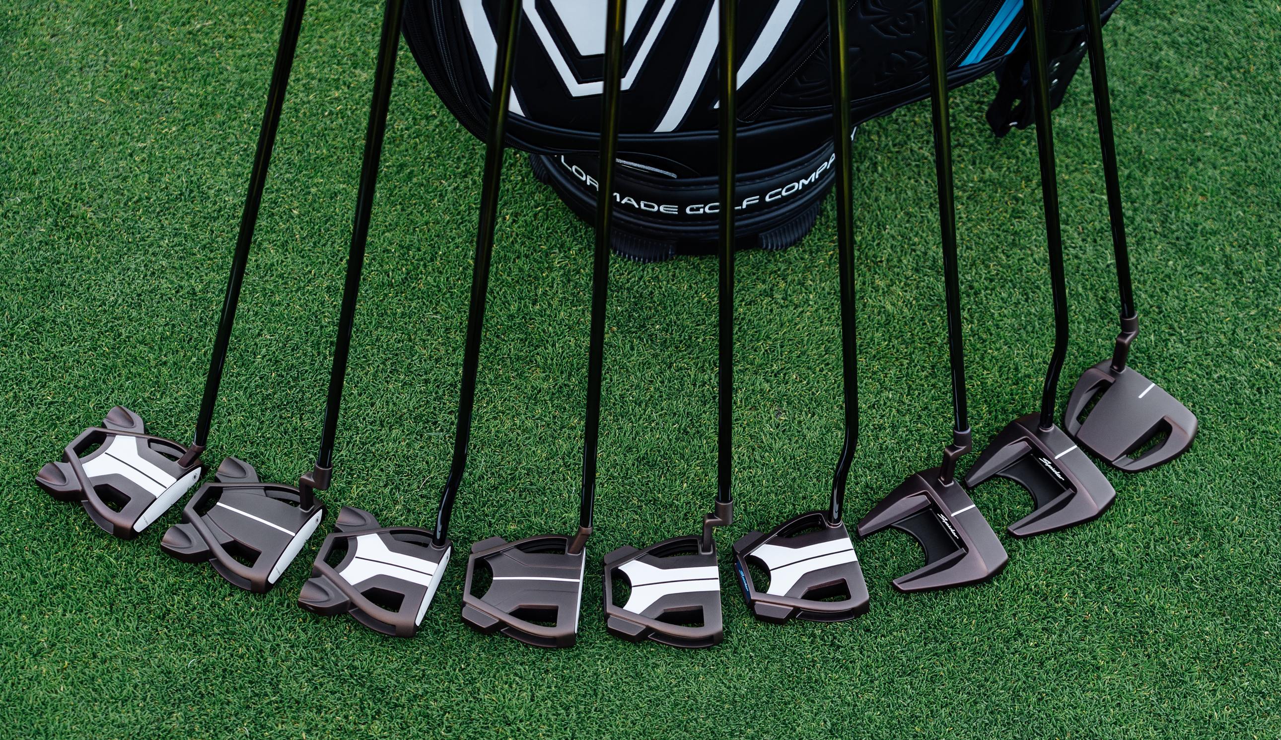 Multiple TaylorMade Spider Tour putters lined up alongside a bag
