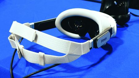 A photo of the Pimax Dream Air VR headset in white on a blue table. The headband, Pimax logo and the lenses are visible. 
