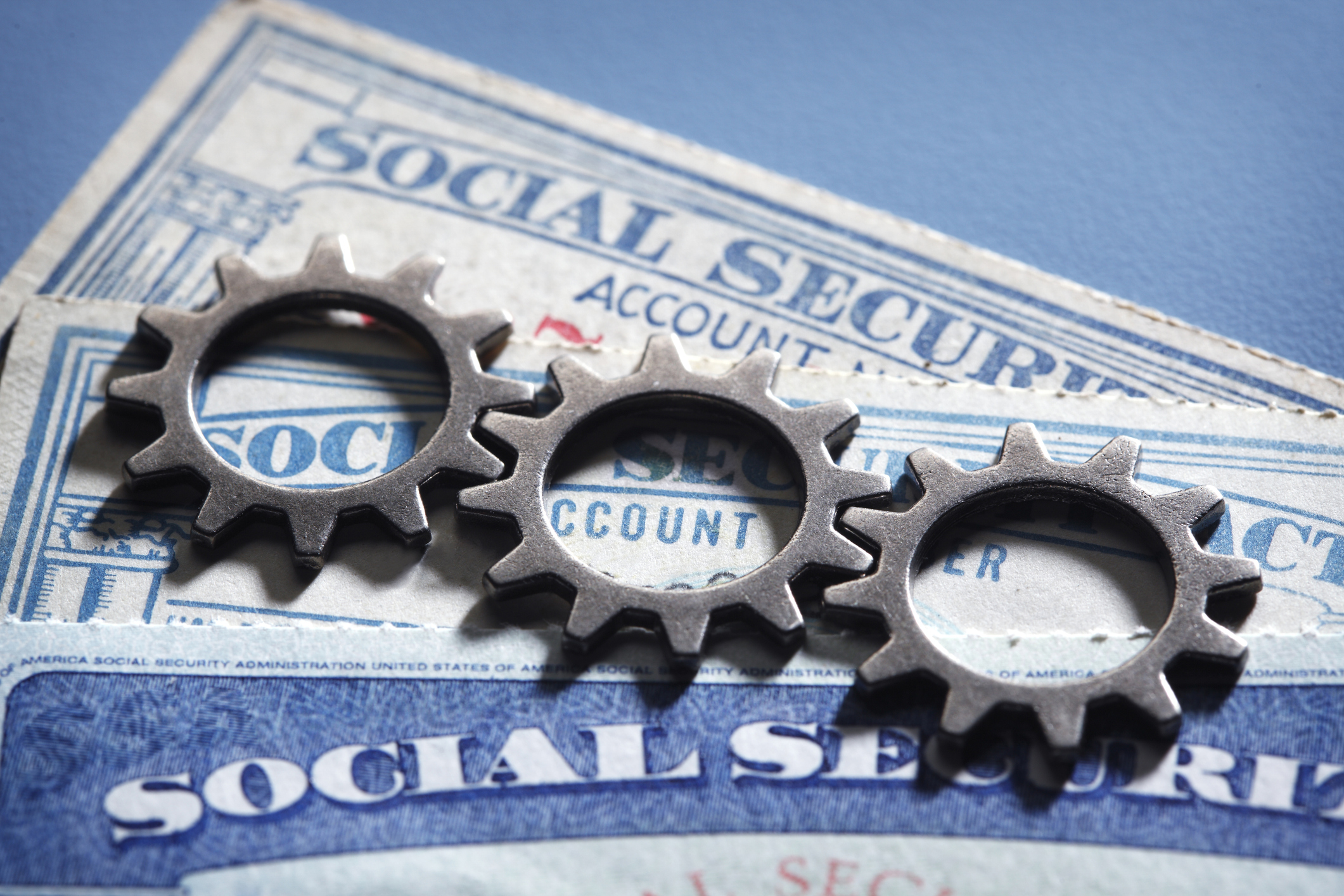 Interlocking gears rest on top of a stack of Social Security cards, representing the complexities of choosing the various options participating in Social Security.
