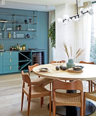 Blue and white kitchen, blue painted accent wall, round wooden dining table and chairs, modern pendant light hanging over table, wooden flooring