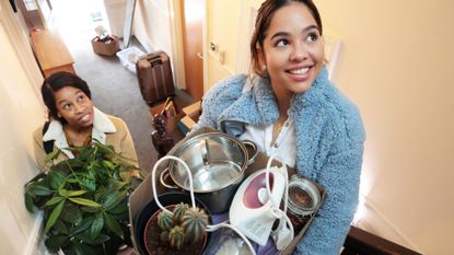 Two women moving into an apartment carrying boxes of possessions and household objects upstairs