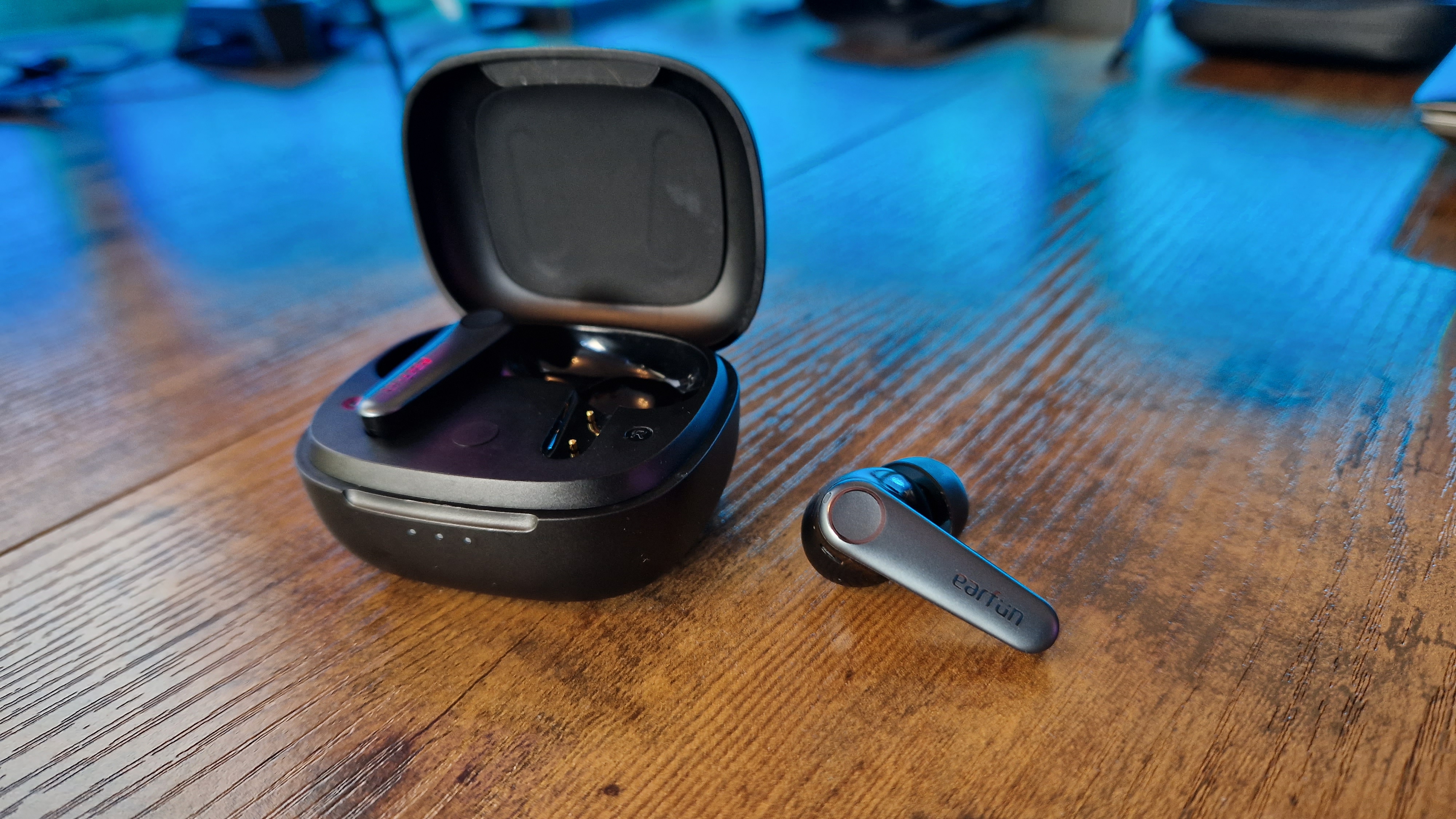 EarFun Air Pro 3 with one earbud outside the case lying on a wooden desk