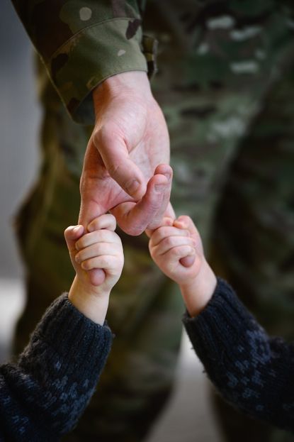 Children holding the hand of a man in military uniform