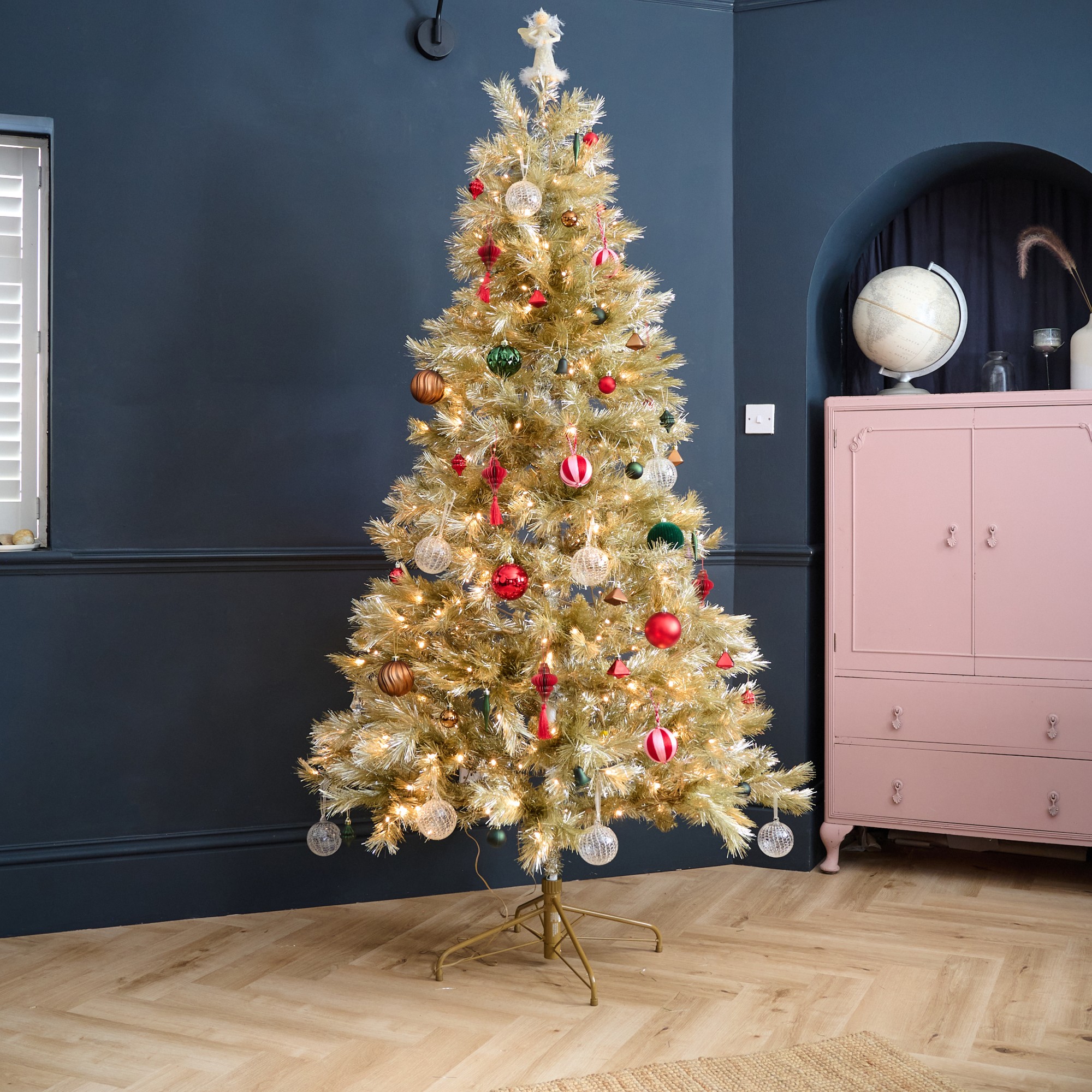 John Lewis' gold Pendleton Pre-lit Christmas Tree decorated with Christmas baubles in a black-painted living room