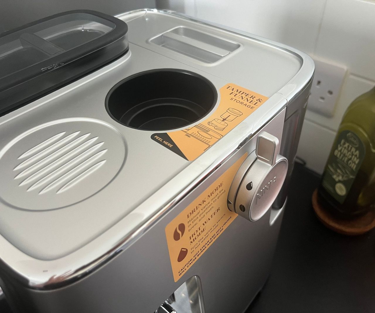 A close up of the sticker explaining the tamper storage compartment and the brew vs hot water dial.
