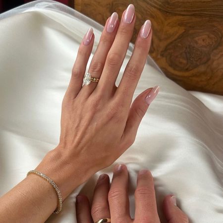 A woman wearing an engagement ring with a shiny pink manicure
