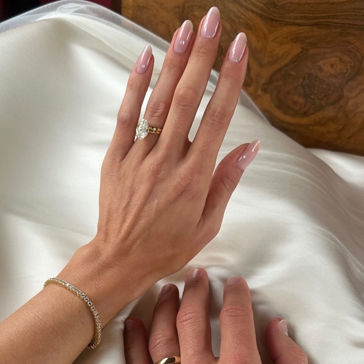 A woman wearing an engagement ring with a shiny pink manicure