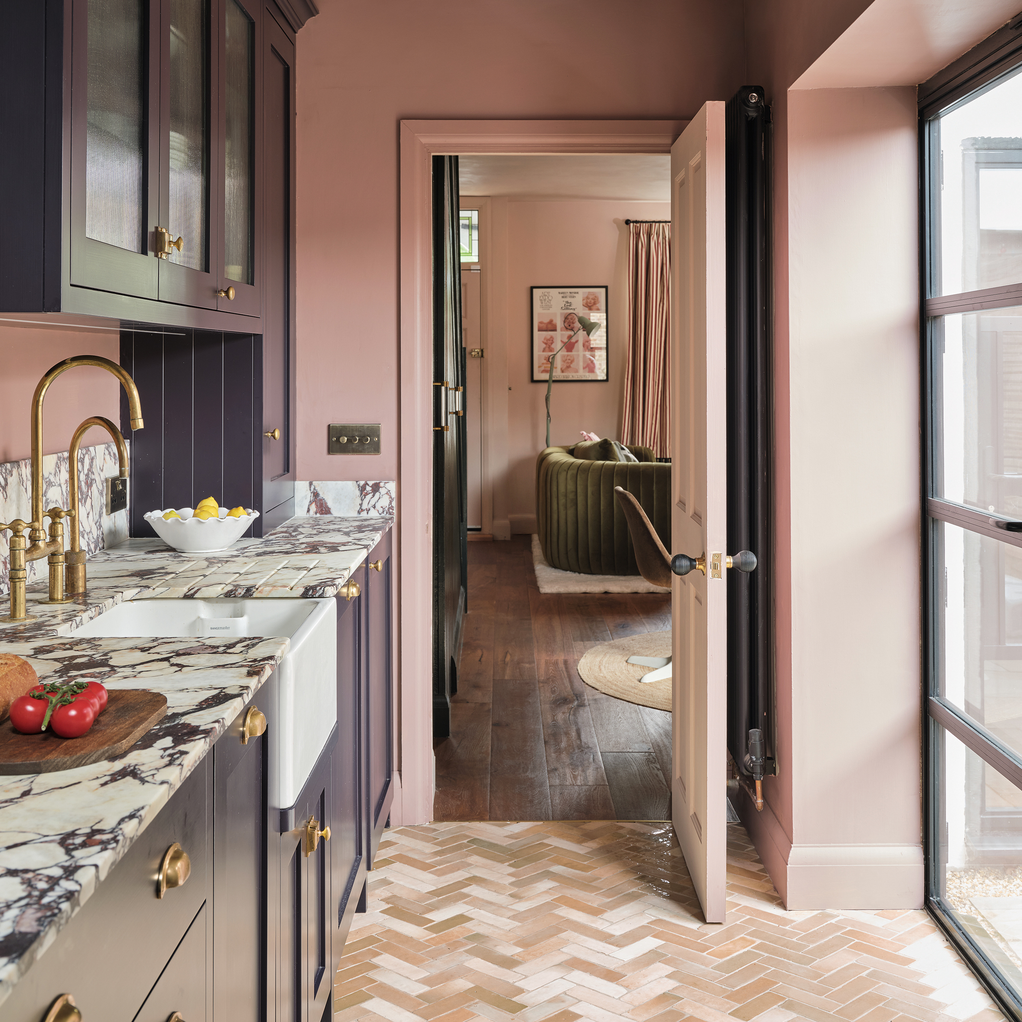 a galley kitchen with purple painted cabinetry and a bold marble countertop, herringbone flooring and glazing on one side