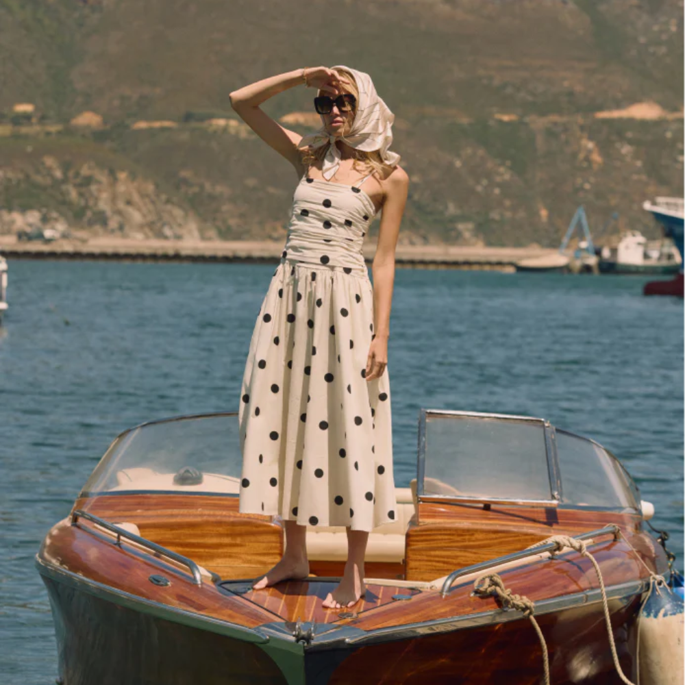 Model stood on a wooden boat weraing a withe and black polkadot bandeau dress sold at nobody's child