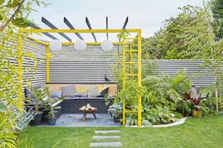 Tropical garden planting with seated area and yellow painted pergola