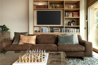 a living room with a brown couch with a tv on the wall behind one of the sofas