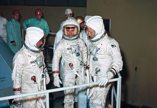 The three crew members for the Apollo-Saturn 204 (AS-204, later renamed Apollo 1) mission check out the couch installation on the Apollo Command Module (CM) at North American's Downey facility. Left to right in their pressurized space suits are astronauts