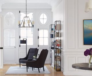 hallway with white paneled walls black chairs and glass doors