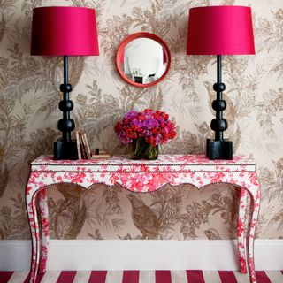 hallway with wallpaper on wall lamps flower vase on wooden table and mirror