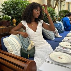 @emmanuellek_ wears a white broderie dress with ruffle sleeves while she sits at a Parisian restaurant