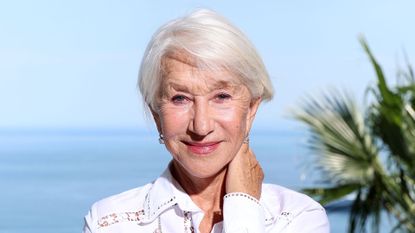 Helen Mirren pictured in front of the sea and blue skies wearing a white blouse with glowing skin and a soft crop haircut