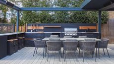 A large outdoor kitchen area with grey metal cabinets and backsplash, and a built in grill, behind a grey roped dining set