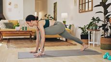 woman performing a deep lunge on an exercise mat in a living room setting. She's facing side on to the camera.