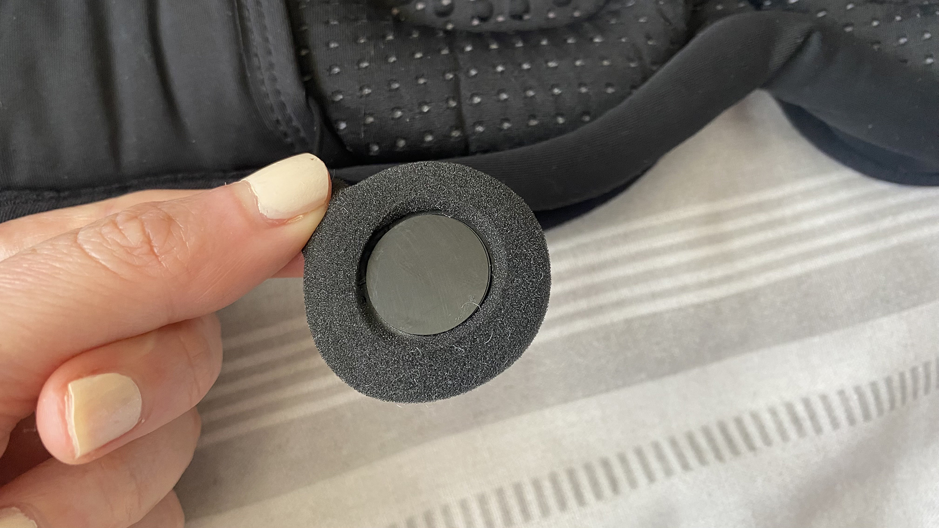 A close up of a hand holding the speakers from the interior of the MUSICOZY Sleep Mask Headphones. The speaker is circular and flat