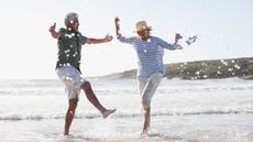 An older couple happily dance in the surf at a beach.