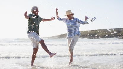 An older couple happily dance in the surf at a beach.
