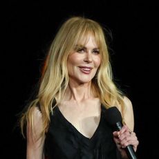 Nicole Kidman has long blonde hair and bangs and wears a slinky black gown to promote 'Practical Magic' with Sandra Bullock