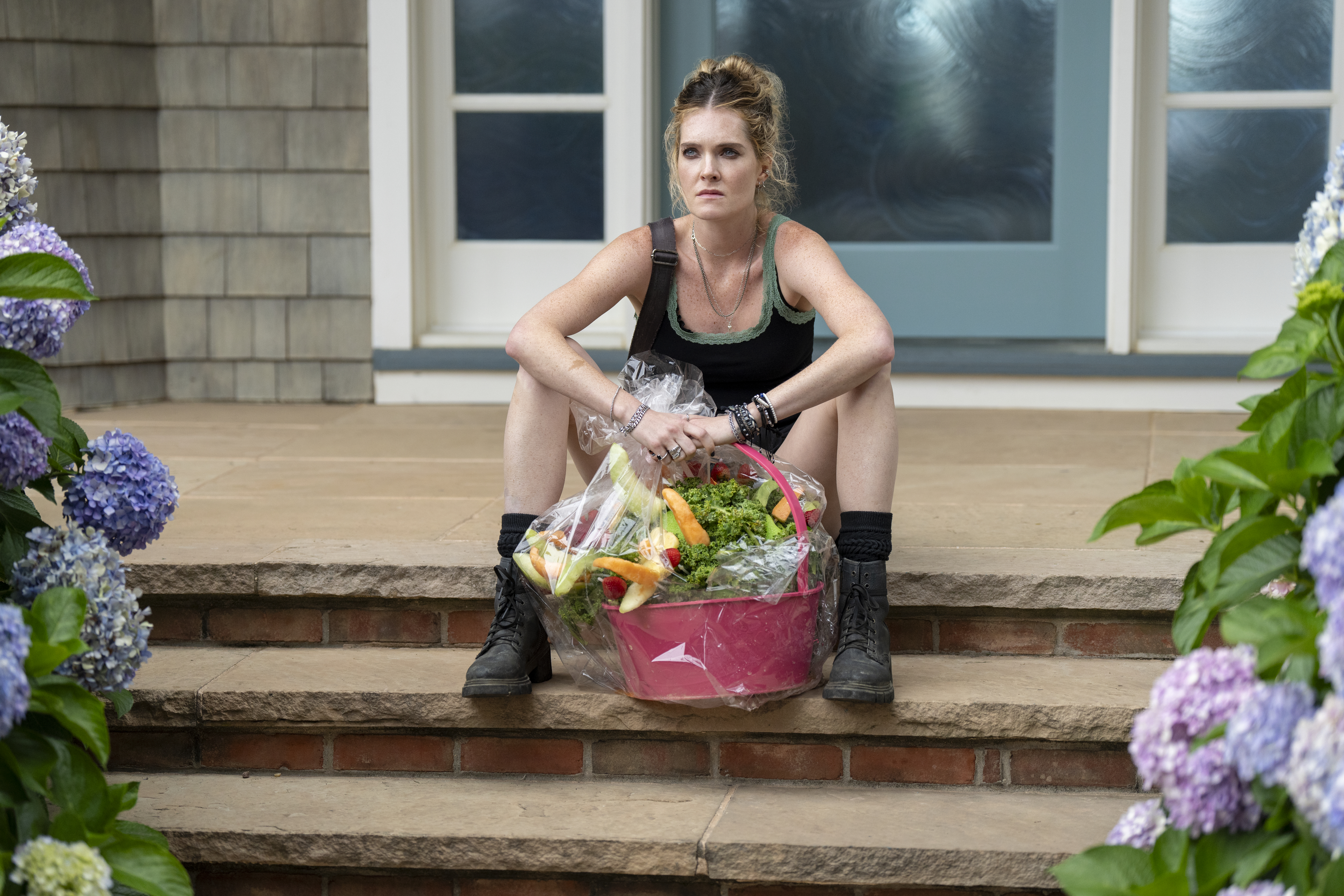 meghann fahy as devon sitting with a fruit basket outside of a house in sirens