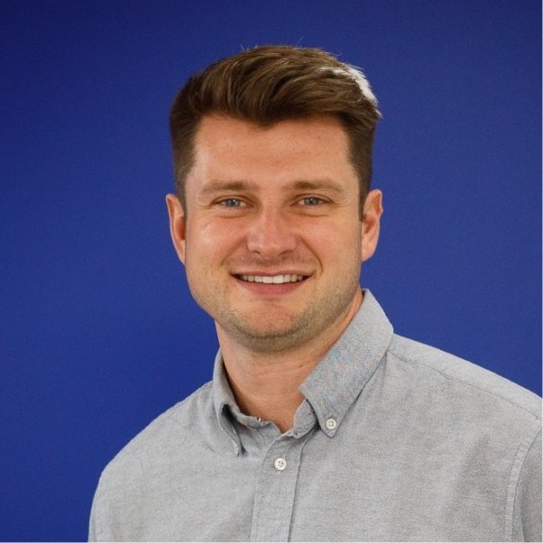 male with short brown hair wearing grey shirt stood against blue blackground