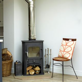 Black wood burner with tall silver chimney in corner of room