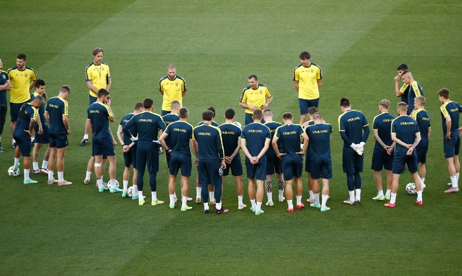 A group of football players in training, gathered in a circle during a team meeting on the field.