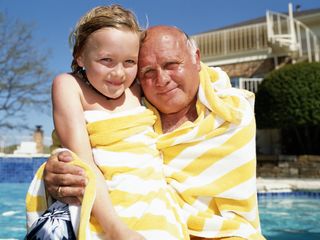 child and grandfather wrapped in towels poolside